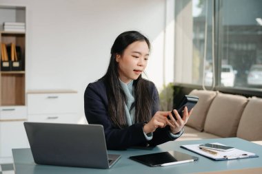 Çalışan not defteri, tablet ve dizüstü bilgisayarla çalışan genç Asyalı iş kadını akıllı telefon, tablet ve dizüstü bilgisayarla konuşuyor video arama vergisi, rapor, muhasebe 