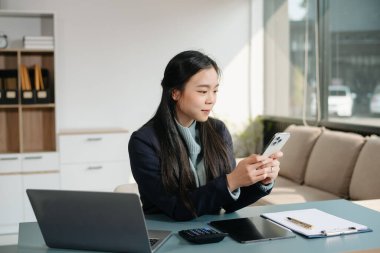 Çalışan not defteri, tablet ve dizüstü bilgisayarla çalışan genç Asyalı iş kadını akıllı telefon, tablet ve dizüstü bilgisayarla konuşuyor video arama vergisi, rapor, muhasebe 