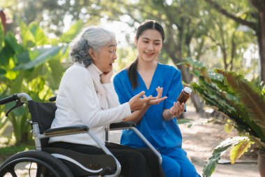 Asyalı yaşlı, yaşlı, yaşlı, tekerlekli sandalyedeki kadın ve Asyalı dikkatli bir bakıcı. Huzurevi hastane bahçesi konsepti