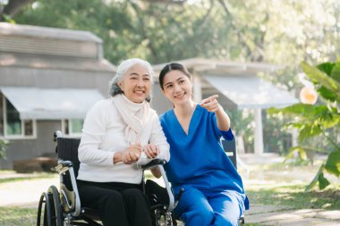 Asyalı genç bakıcı hemşire yaşlı bir erkeğin dışarıda yürümesini destekliyor. Uzman doktorlar yaşlı yetişkinlere yardım eder ve onlarla ilgilenir. Huzurevi hastanesi bahçesi