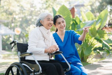 Asyalı genç bakıcı hemşire yaşlı bir erkeğin dışarıda yürümesini destekliyor. Uzman doktorlar yaşlı yetişkinlere yardım eder ve onlarla ilgilenir. Huzurevi hastanesi bahçesi