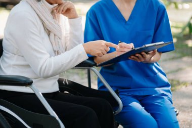 Asyalı genç bakıcı hemşire yaşlı bir erkeğin dışarıda yürümesini destekliyor. Uzman doktorlar yaşlı yetişkinlere yardım eder ve onlarla ilgilenir. Huzurevi hastanesi bahçesi