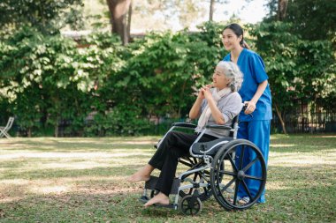 Asyalı fizyoterapist, yaşlı bir kadının egzersiz sırasında kollarını esnetmesine yardım ediyor. Hasta sırtı problemli bir halterle, ellerindeki dambılla. Huzurevi hastane bahçesi konsepti