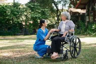 Asyalı fizyoterapist, yaşlı bir kadının egzersiz sırasında kollarını esnetmesine yardım ediyor. Hasta sırtı problemli bir halterle, ellerindeki dambılla. Huzurevi hastane bahçesi konsepti
