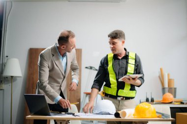 Professional collaboration in architecture. Two engineers work on construction plans, using tools like laptops, tablets, and scale models. Perfect for depicting teamwork 