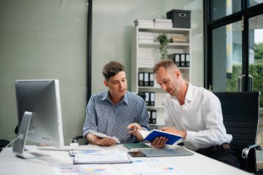 İki iş adamı akıllı telefondan konuşuyor ve ofiste dizüstü bilgisayar kullanıyorlar.
