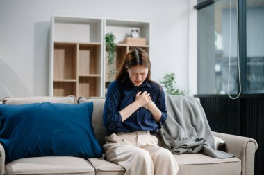 Kanepede battaniyeyle kaplanmış, grip belirtileri gösteren genç bir Asyalı kadın. Hastalık, sağlık ve iyileşme kavramı. Evde kal, sağlıklı kal.