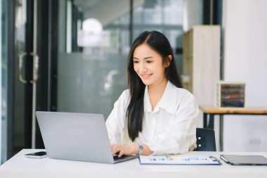 Çalışan not defteri, tablet ve dizüstü bilgisayarla çalışan genç Asyalı iş kadını akıllı telefon, tablet ve dizüstü bilgisayarla konuşuyor. Video arama vergisi, rapor, muhasebe
