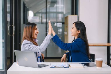 Asyalı iş arkadaşları sunar ve açıklar ve dizüstü bilgisayar ve tablet kullanır. Takım çalışması, finansal pazarlama ekibi, modern ofis odasında otururken