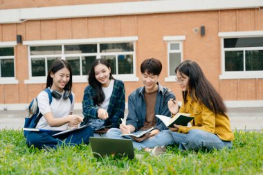 Genç Asyalı üniversite öğrencileri ve bir kız öğrenci grubu sabahları arkadaşlarıyla kampüs parkında çalışıyor. Eğitim kavramı 