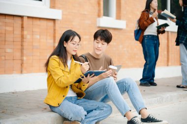 Genç Asyalı üniversite öğrencileri ve bir kız öğrenci grubu sabahları arkadaşlarıyla kampüs parkında çalışıyor. Eğitim kavramı 