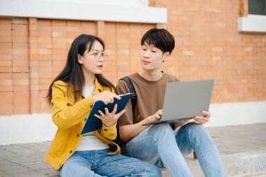 Asyalı öğrenciler kampüs parkını inceliyor. Gençler birlikte vakit geçiriyorlar. Kitap okumak, dizüstü bilgisayarla çalışmak ve merdivenlerde oturmak.