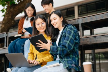 Genç Asyalı üniversite öğrencileri ve bir kız öğrenci grubu sabahları arkadaşlarıyla kampüs parkında çalışıyor. Eğitim kavramı 