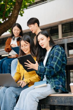 Genç Asyalı üniversite öğrencileri ve bir kız öğrenci grubu sabahları arkadaşlarıyla kampüs parkında çalışıyor. Eğitim kavramı 
