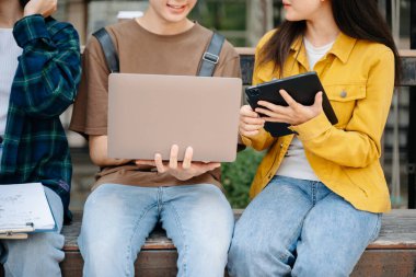 Genç Asyalı üniversite öğrencileri ve bir kız öğrenci grubu sabahları arkadaşlarıyla kampüs parkında çalışıyor. Eğitim kavramı 