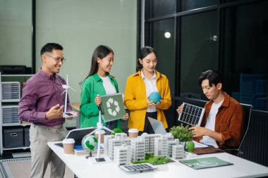 Asyalı profesyoneller ofiste rüzgar türbinleri, güneş panelleri ve çevre dostu modellerle sürdürülebilir enerji çözümleri üzerinde işbirliği yapmaktadırlar.