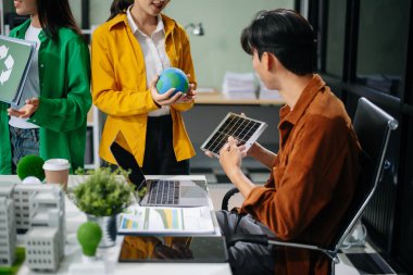 Asyalı profesyoneller ofiste rüzgar türbinleri, güneş panelleri ve çevre dostu modellerle sürdürülebilir enerji çözümleri üzerinde işbirliği yapmaktadırlar.