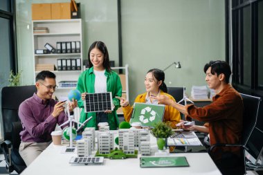 Asyalı profesyoneller ofiste rüzgar türbinleri, güneş panelleri ve çevre dostu modellerle sürdürülebilir enerji çözümleri üzerinde işbirliği yapmaktadırlar.