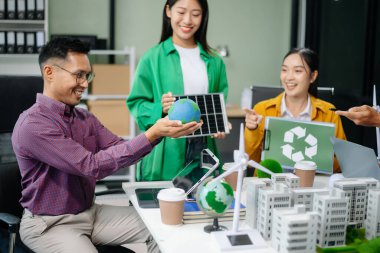 Asyalı profesyoneller ofiste rüzgar türbinleri, güneş panelleri ve çevre dostu modellerle sürdürülebilir enerji çözümleri üzerinde işbirliği yapmaktadırlar.