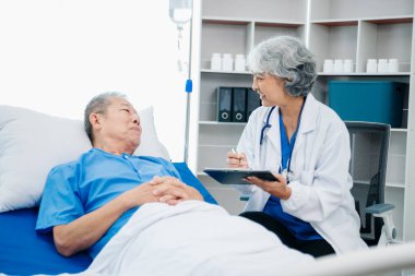 Beyaz takım elbiseli Asyalı doktor, hastanede ya da klinikte salin solüsyonu alan Asyalı yaşlıları ve yatakta yatan hastaları tartışırken not alıyor..