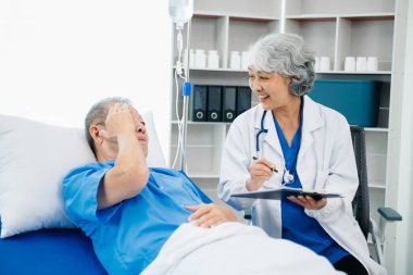 Beyaz takım elbiseli Asyalı doktor, hastanede ya da klinikte salin solüsyonu alan Asyalı yaşlıları ve yatakta yatan hastaları tartışırken not alıyor..