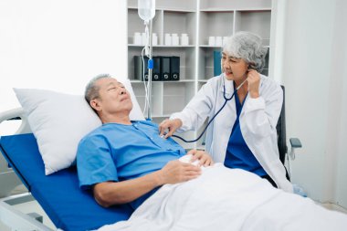 Beyaz takım elbiseli Asyalı doktor, hastanede ya da klinikte salin solüsyonu alan Asyalı yaşlıları ve yatakta yatan hastaları tartışırken not alıyor..