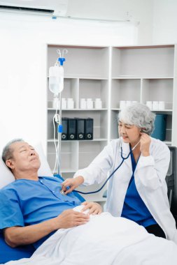 Beyaz takım elbiseli Asyalı doktor, hastanede ya da klinikte salin solüsyonu alan Asyalı yaşlıları ve yatakta yatan hastaları tartışırken not alıyor..