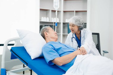 Beyaz takım elbiseli Asyalı doktor, hastanede ya da klinikte salin solüsyonu alan Asyalı yaşlıları ve yatakta yatan hastaları tartışırken not alıyor..