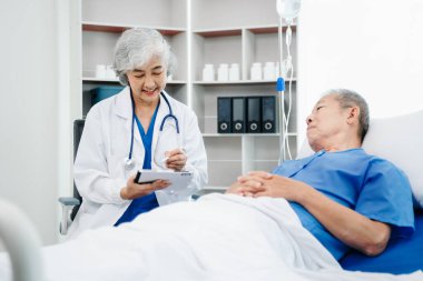 Beyaz takım elbiseli Asyalı doktor, hastanede ya da klinikte salin solüsyonu alan Asyalı yaşlıları ve yatakta yatan hastaları tartışırken not alıyor..