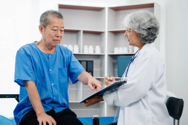 Beyaz takım elbiseli Asyalı doktor, hastanede ya da klinikte salin solüsyonu alan Asyalı yaşlıları ve yatakta yatan hastaları tartışırken not alıyor..