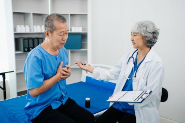 Beyaz takım elbiseli Asyalı doktor, hastanede ya da klinikte salin solüsyonu alan Asyalı yaşlıları ve yatakta yatan hastaları tartışırken not alıyor..