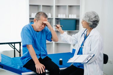 Beyaz takım elbiseli Asyalı doktor, hastanede ya da klinikte salin solüsyonu alan Asyalı yaşlıları ve yatakta yatan hastaları tartışırken not alıyor..