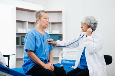 Beyaz takım elbiseli Asyalı doktor, hastanede ya da klinikte salin solüsyonu alan Asyalı yaşlıları ve yatakta yatan hastaları tartışırken not alıyor..