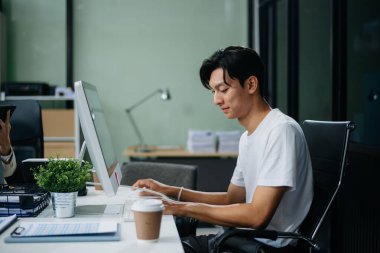 Modern ofiste laptopla, tabletle çalışan ve kağıda not alan genç bir iş adamı..