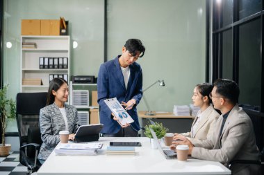 Modern bir ofiste Asyalı profesyoneller arasındaki takım çalışması ve işbirliği, kurumsal kültür, yenilik ve verimliliği gözler önüne seriyor