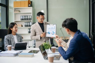 Modern bir ofiste Asyalı profesyoneller arasındaki takım çalışması ve işbirliği, kurumsal kültür, yenilik ve verimliliği gözler önüne seriyor