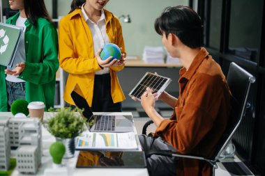 Asyalı profesyoneller ofiste rüzgar türbinleri, güneş panelleri ve çevre dostu modellerle sürdürülebilir enerji çözümleri üzerinde işbirliği yapmaktadırlar.