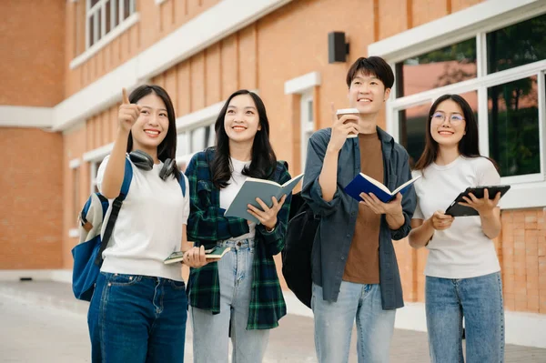 Genç Asyalı üniversite öğrencileri ve bir kız öğrenci grubu sabahları arkadaşlarıyla kampüs parkında çalışıyor. Eğitim kavramı 
