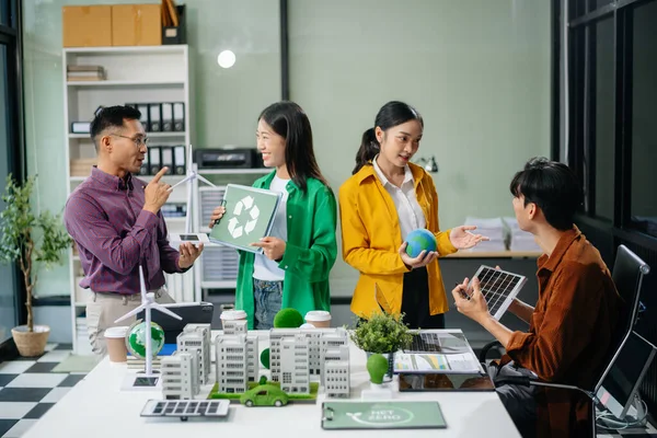 Asyalı profesyoneller ofiste rüzgar türbinleri, güneş panelleri ve çevre dostu modellerle sürdürülebilir enerji çözümleri üzerinde işbirliği yapmaktadırlar.