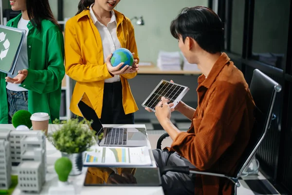 Asyalı profesyoneller ofiste rüzgar türbinleri, güneş panelleri ve çevre dostu modellerle sürdürülebilir enerji çözümleri üzerinde işbirliği yapmaktadırlar.