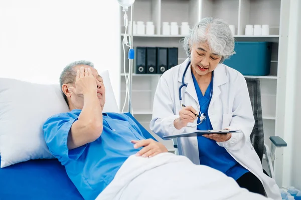 Beyaz takım elbiseli Asyalı doktor, hastanede ya da klinikte salin solüsyonu alan Asyalı yaşlıları ve yatakta yatan hastaları tartışırken not alıyor..