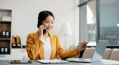 Confident Asian woman with a smile standing holding notepad and tablet at the modern office.