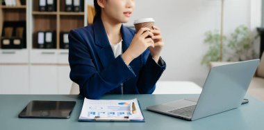 Confident Asian woman with a smile standing holding notepad and tablet at the modern office.