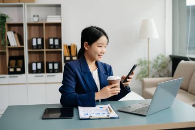 Confident Asian woman with a smile standing holding notepad and tablet at the modern office.