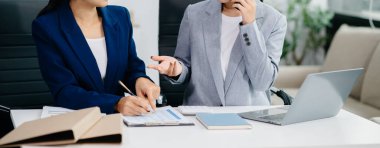 İki iş adamı akıllı telefondan konuşuyor ve ofiste dizüstü bilgisayar kullanıyorlar.