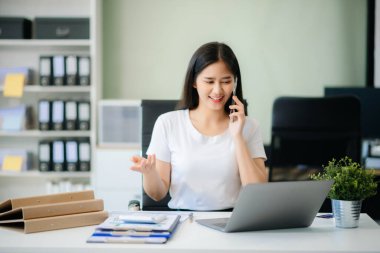 Kendine güvenen iş uzmanı, gülümseyen, dizüstü bilgisayarda yazan ve dijital tableti yaratıcı ofiste tutan çekici genç bir kadın.