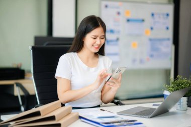 Kendine güvenen iş uzmanı, gülümseyen, dizüstü bilgisayarda yazan ve dijital tableti yaratıcı ofiste tutan çekici genç bir kadın.