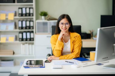 Kendine güvenen iş uzmanı çekici, gülümseyen genç bir kadın yaratıcı ofiste elinde dijital tablet tutuyor.