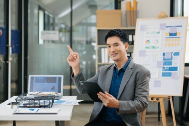 Genç ve çekici Asyalı ofis çalışanı takım elbiseleri ofiste kameraya gülümsüyor.