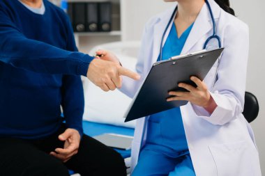 Modern bir klinikte muayene odasında oturan yaşlı bir erkek hastayla tedaviyi tartışan ve gülen bir doktor.